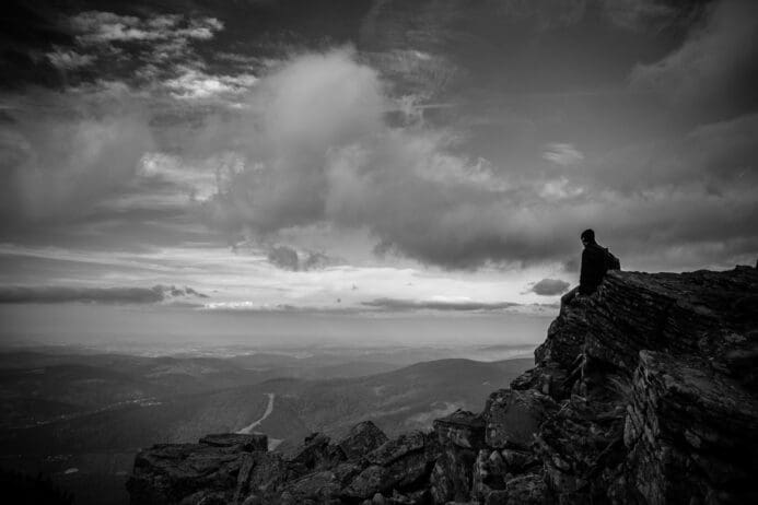 person looking off into the stormy horizon in black and white while standing on a cliff