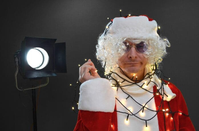 A thin Santa wearing beatles style glasses in front of camera lighting on a black background this santa has no beard