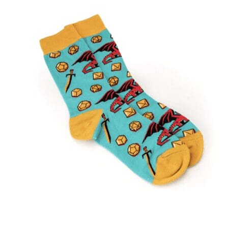 The image shows a pair of colorful socks with a fantasy theme. The socks are primarily turquoise with mustard yellow accents at the toes, heels, and cuffs. The pattern on the socks includes images of red dragons, swords, and gold polyhedral dice, resembling a design inspired by tabletop role-playing games.